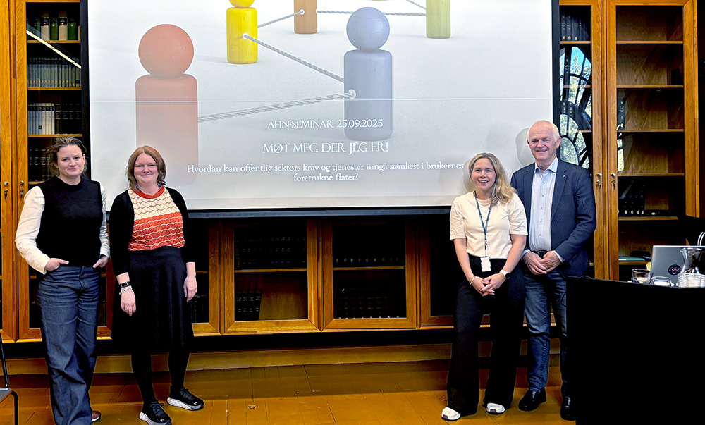 Fire personer står foran en skjerm med illustrasjon som viser samarbeid.